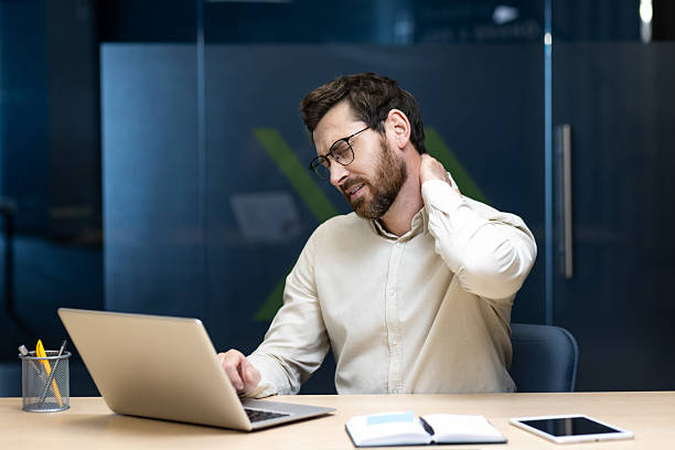 一名久坐於辦公桌前工作、正按摩因使用電腦導致肩頸痠痛的白領男性。